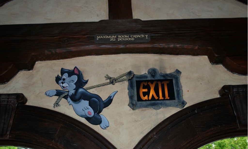 As you exit the Village Haus Restaurant, you will see an image of Fiagro painted on the wall. He has a rope over his shoulder, which is connected to the illuminated exit sign, to give the appearance that his is pulling it along. I have heard a few different versions of the story, but the gist is that Disney's Imagineers needed a clever way to obscure the fact that the exit sign was off center.