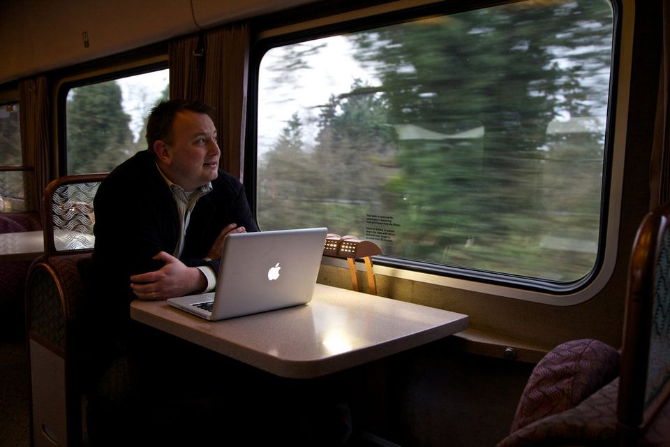 A man riding on a train with a MacBook Pro on a table